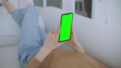 Close-up-shot-of-green-screen-template-smartphone-in-female-hands-at-home-girl-is-watching-content-without-touching-gadget-screen.-Modern-technology-and-information-concept.